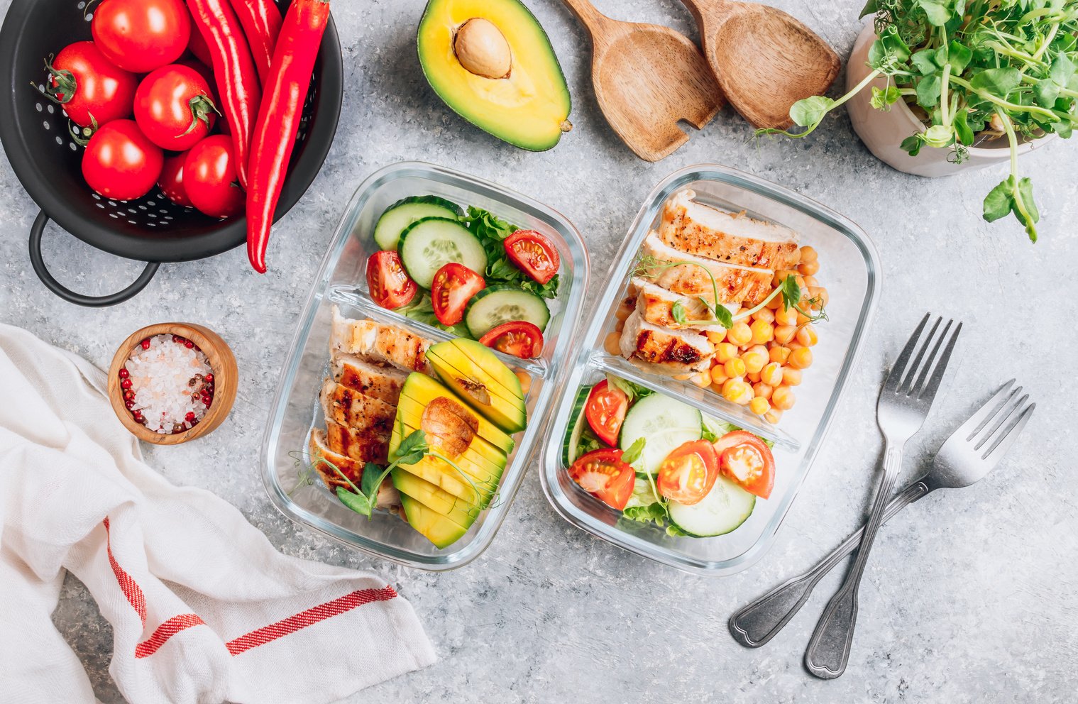 Healthy meal prep containers with chickpeas, chicken, tomatoes, cucumbers and avocados. Healthy lunch in glass containers on light gray background. Zero waste concept. Selective focus.